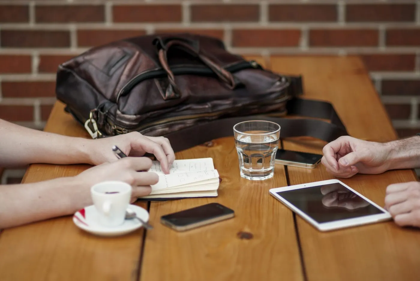 Duas pessoas em uma mesa com tablet, caderno e café, conversando sobre as perguntas antes de contratar um site