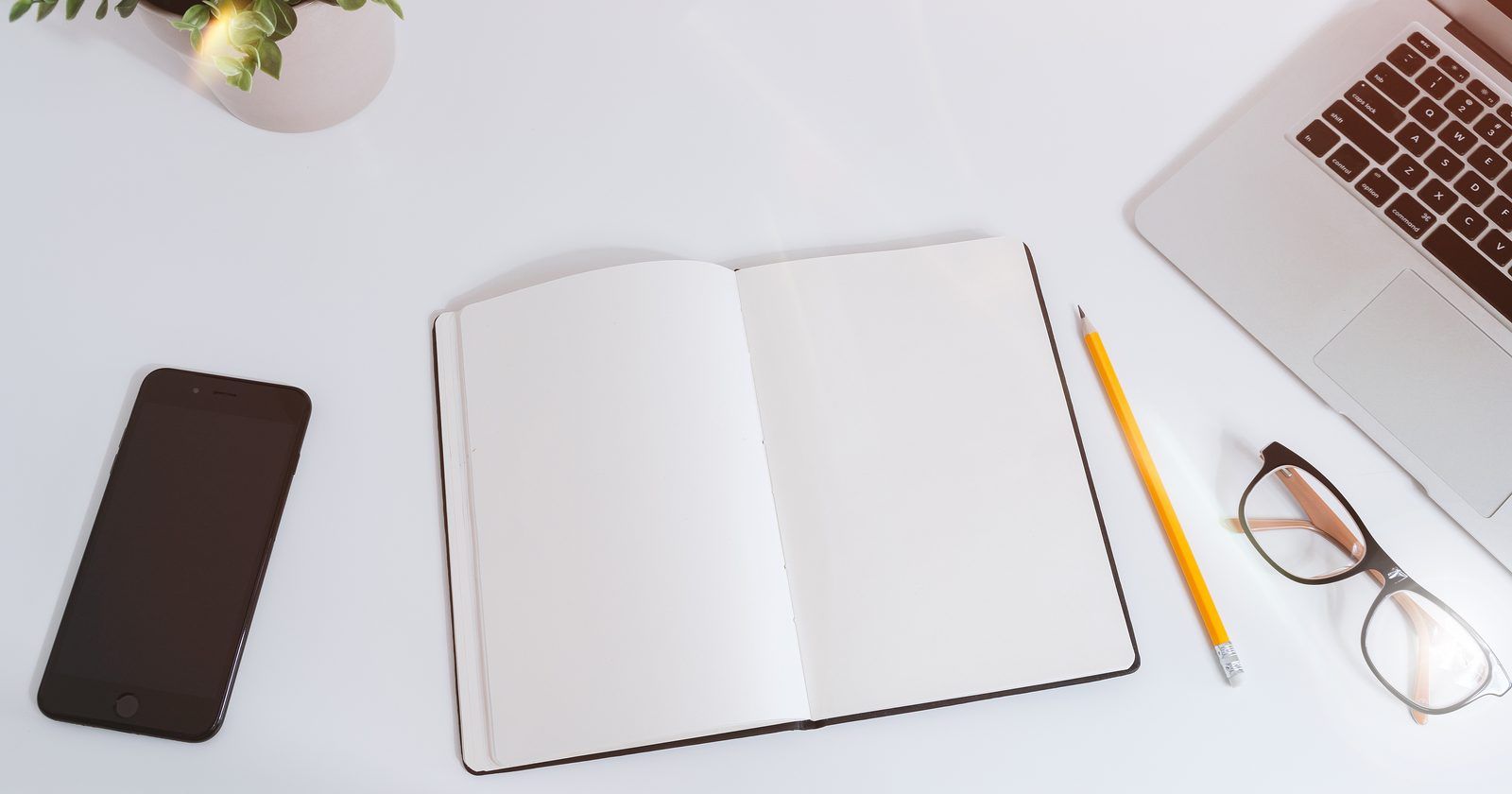 Desk with an open notebook, a pencil, a phone and a laptop, set up for planning the cost of a small business website